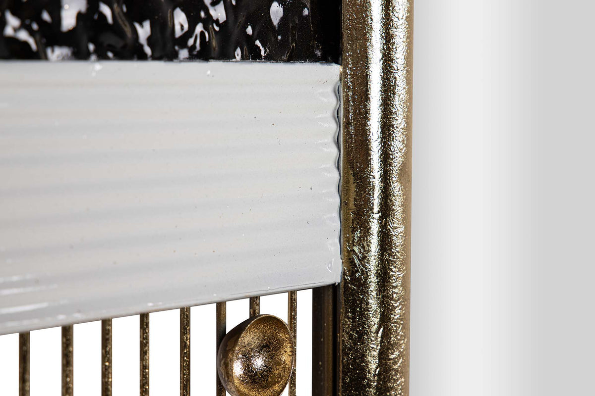 Close-up detail of a decorative wall mirror or panel with a white ribbed lower section, vertical gold-toned metal bars, a round gold finial, and a textured metallic frame | KULORI Malta & Gozo