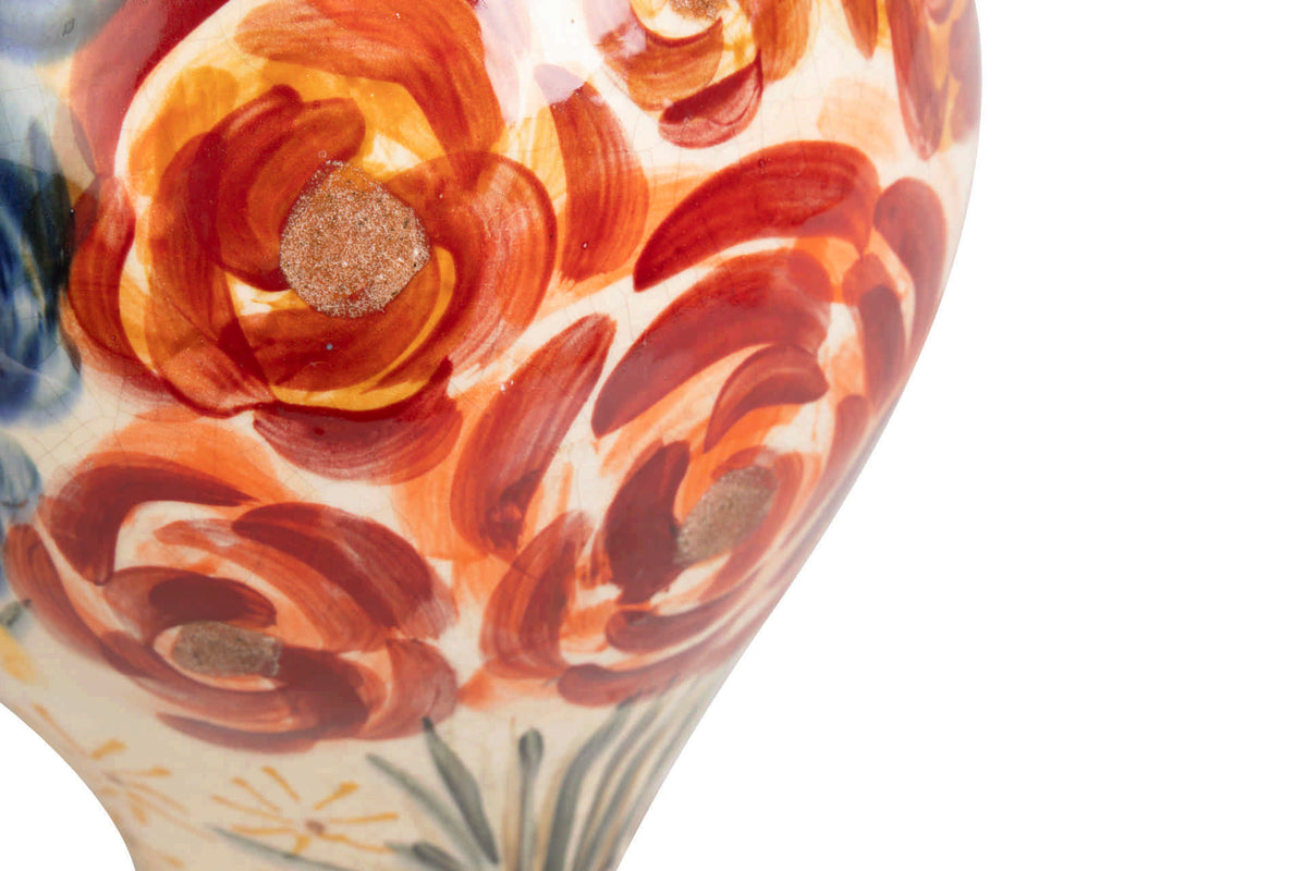 Close-up of a ceramic vase featuring hand-painted floral motifs in warm orange, red, and brown tones on an off-white background, with a small blue accent visible on the left edge.