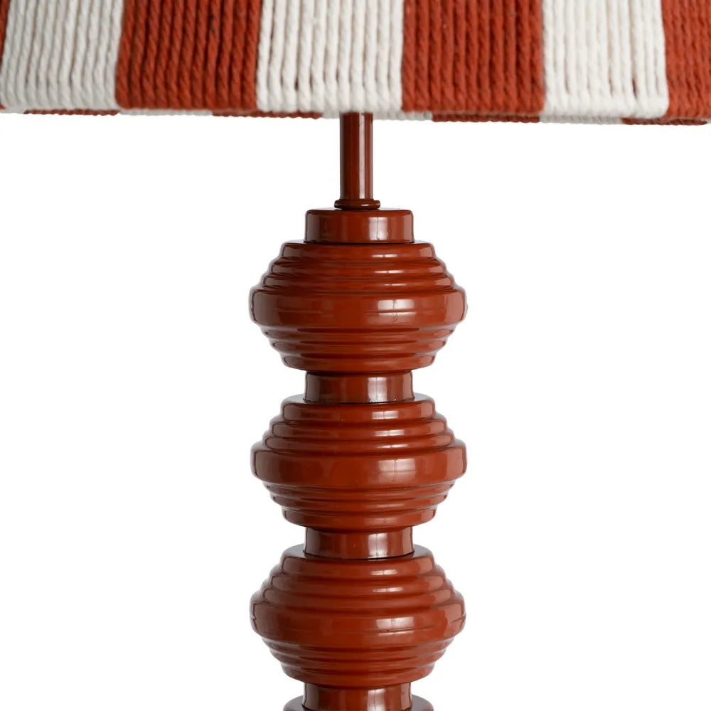 Close-up of a table lamp with a glossy reddish-brown turned metal spindle base and a striped fabric shade in rust red and off-white | KULORI