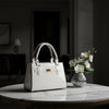 A glossy white patent ceramic handbag with structured double top handles, a front strap detail | KULORI