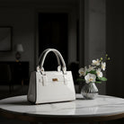 A glossy white patent ceramic handbag with structured double top handles, a front strap detail | KULORI