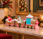 A festive Christmas train decoration with gingerbread carriages and a pink locomotive, styled on a marble console table with holiday greenery, a mirror, and warm ambient lights in the background.