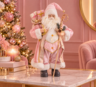 A Santa Claus figurine or decorative statue stands on a marble table in a pink holiday room. The Santa outfit is predominantly pink with white fur trim, gold accents, and black boots.
