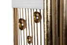 Close-up of a decorative gold-toned metal wall hanging or sculpture with vertical bars, a white rectangular top panel, and three dome-shaped metallic accents | KULORI Malta & Gozo