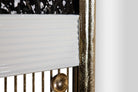 Close-up detail of a decorative wall mirror or panel with a white ribbed lower section, vertical gold-toned metal bars, a round gold finial, and a textured metallic frame | KULORI Malta & Gozo