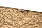 Close-up of a textured metallic gold clutch or envelope-style bag corner with a keyhole-shaped metal clasp on a plain white background | KULORI Malta & Gozo