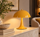 A glossy mustard yellow mushroom-shaped table lamp sits on a light stone console table in a warmly lit living room setting | KULORI Malta & Gozo