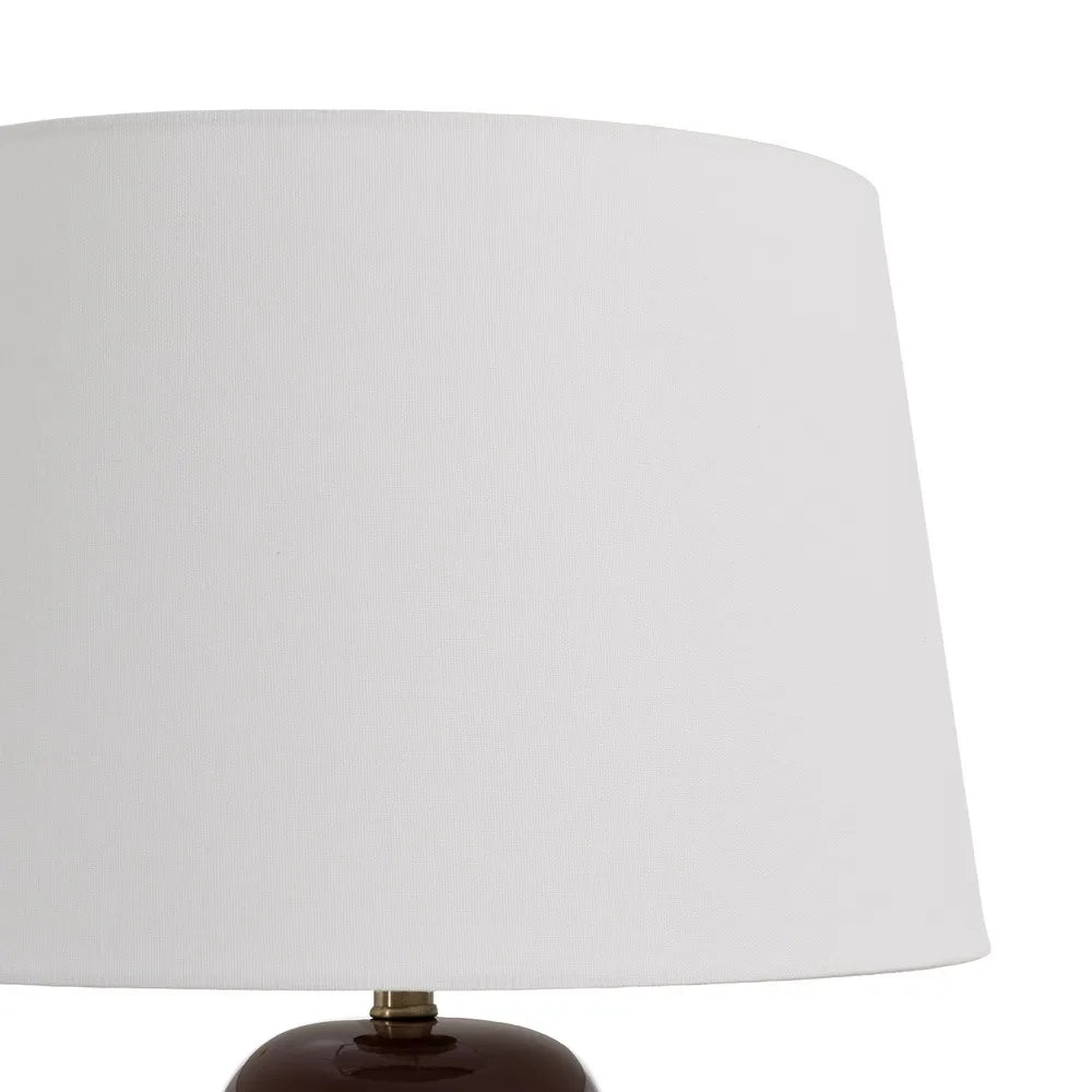 A close-up of a table lamp featuring a large white fabric drum shade and a glossy dark brown ceramic base with a small brass finial | KULORI Malta & Gozo