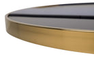 Close-up of a round table showing a polished gold metal frame and a dark, likely black | KULORI Malta & Gozo