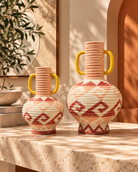 Two decorative woven ceramic vases with yellow handles and red geometric patterns, displayed on a stone table in a warm, sunlit interior setting | KULORI Malta & Gozo