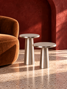 Two modern metallic side tables with tapered silver pedestal legs and circular tops, styled in a warm interior with a terracotta wall and terrazzo floor | KULORI Malta & Gozo
