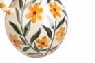 Close-up of a ceramic vessel with a glossy cream glaze, decorated with a hand-painted floral pattern of yellow flowers with red centers and green leaves.