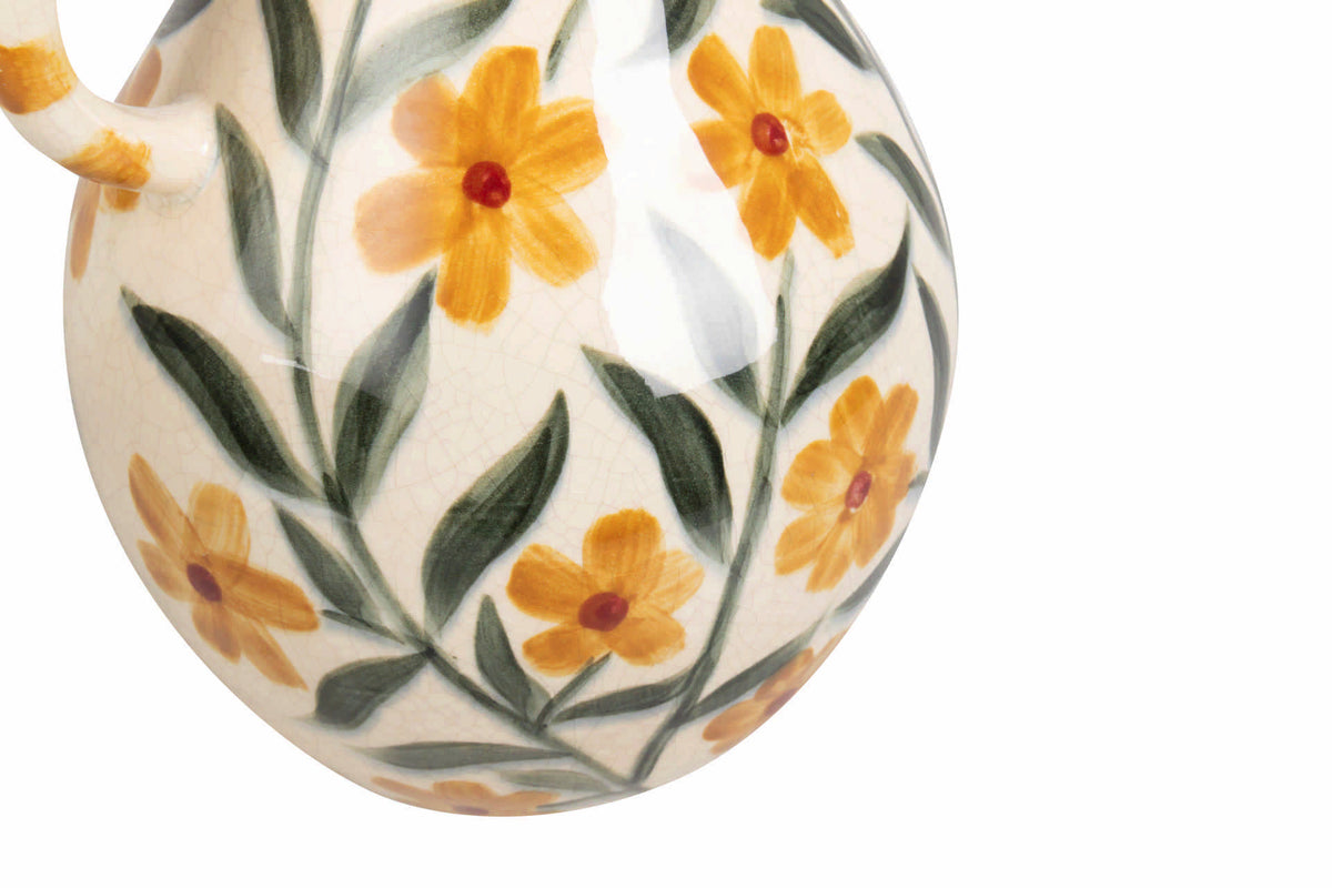 Close-up of a ceramic vessel with a glossy cream glaze, decorated with a hand-painted floral pattern of yellow flowers with red centers and green leaves.