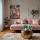 A colourful framed wall art print depicting a tropical hillside village with pink buildings and palm trees | KULORI