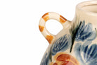 Close-up of a ceramic pitcher with a loop handle, decorated with blue floral patterns and orange-brown accents